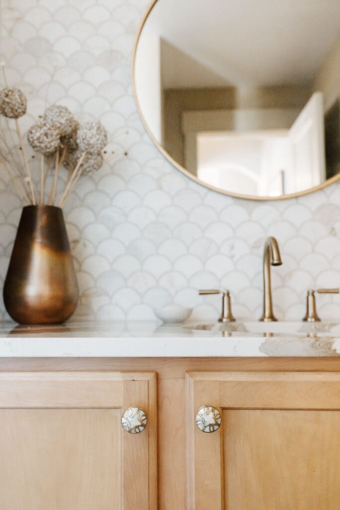 Powder bathroom with warm wood, Mother-of-Pearl hardware, copper accessories, brass plumbing and lighting fixtures, Cambria quartz counter, and marble wainscot tile