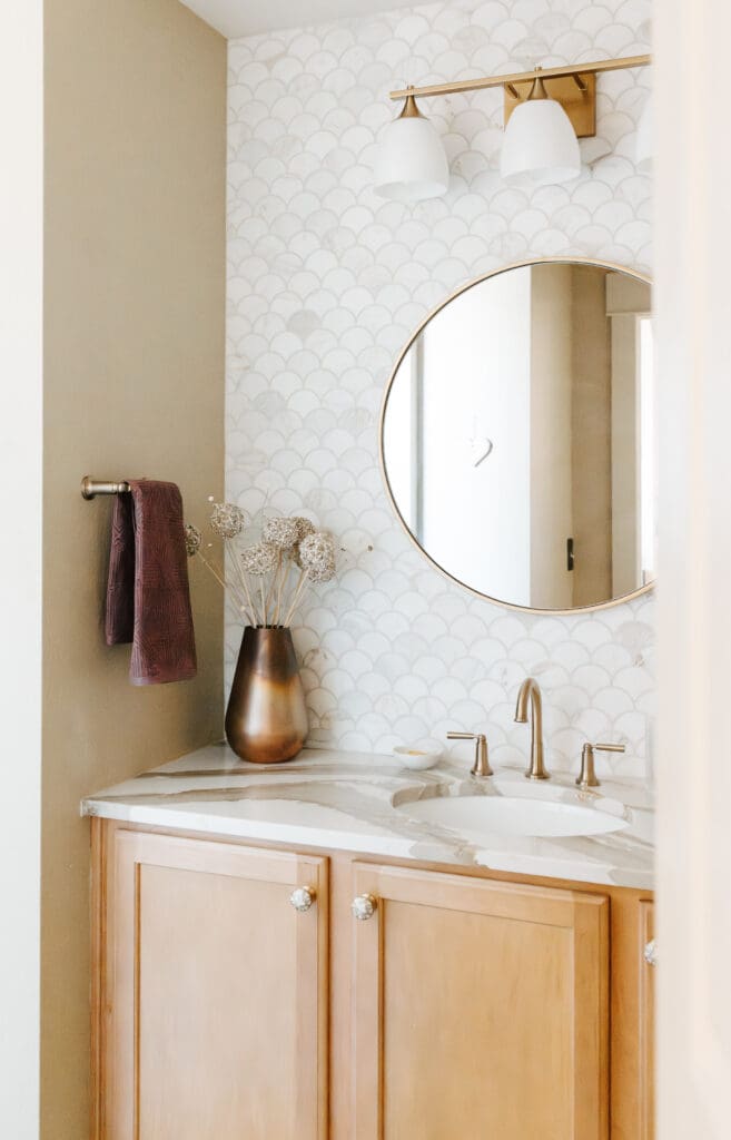 Powder bathroom with warm wood, Mother-of-Pearl hardware, copper accessories, brass plumbing and lighting fixtures, Cambria quartz counter, and marble wainscot tile