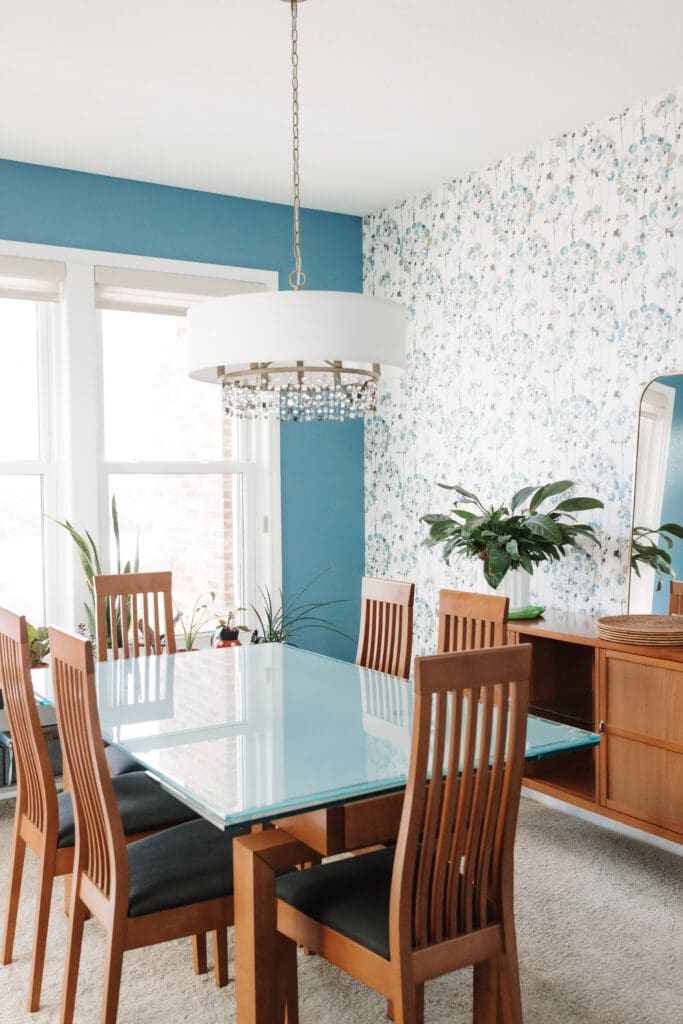 Dining room with biophilia, floral wallpaper, teal wall paint, drum fixtures with crystal details, and warm wood furniture