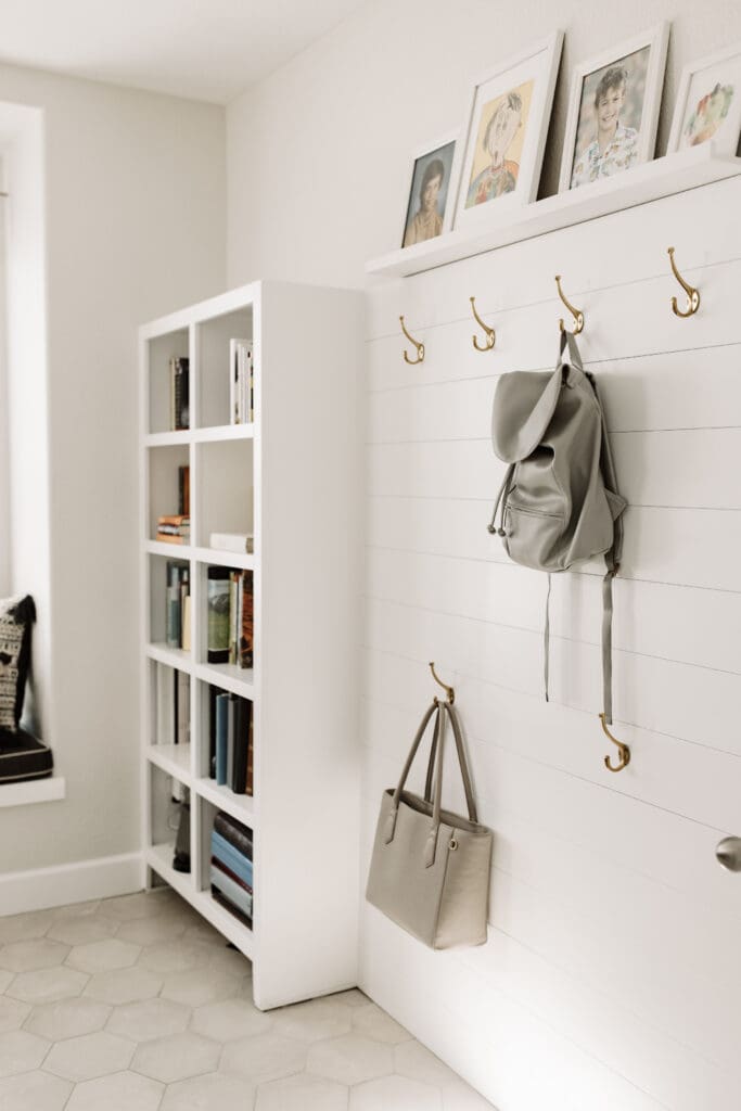 Built-in bookshelf and mud room wall with white wainscoting and brass Restoration Hardware hooks