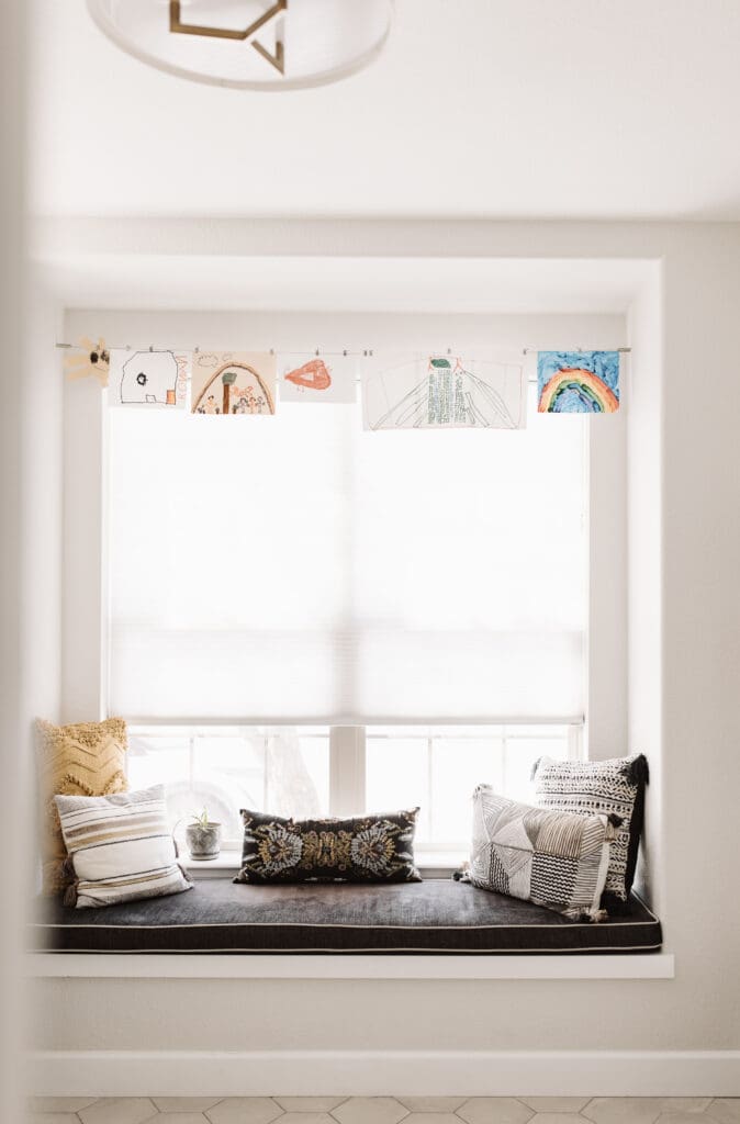 Window seat with children's artwork and colorful, textural pillows and black Kravet cushion.