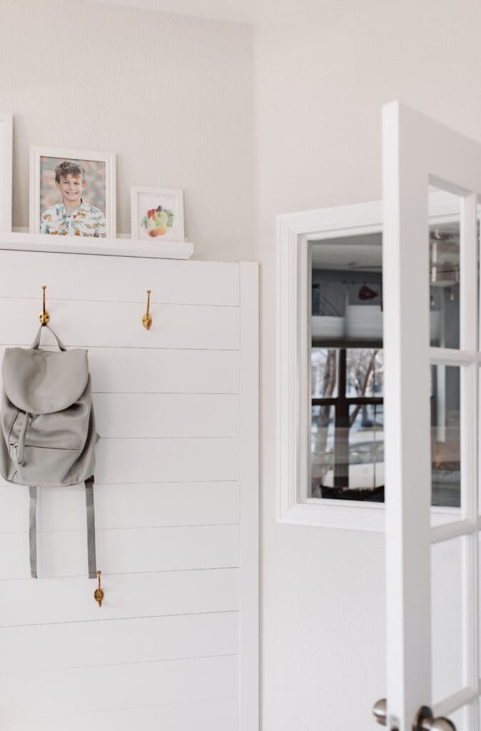 Mud room wall with white wainscoting, picture shelf, and brass Restoration Hardware hooks