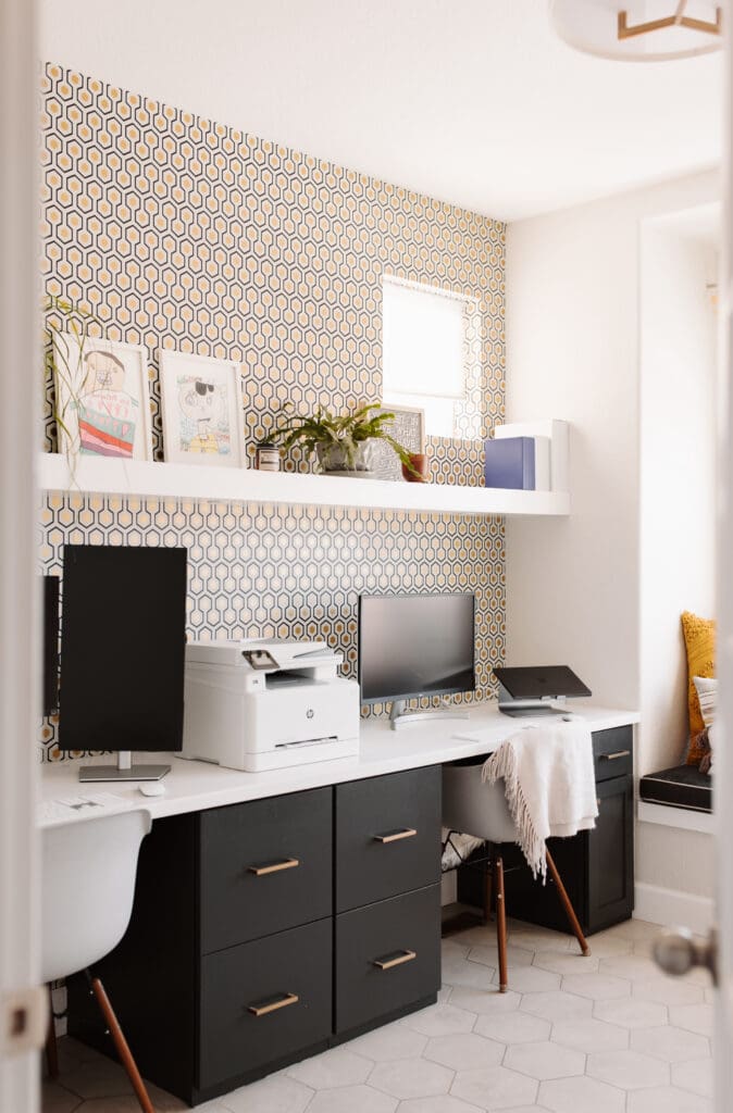 Double office with natural light, geometric metallic wallpaper, charcoal cabinetry, box shelf, and biophilia.