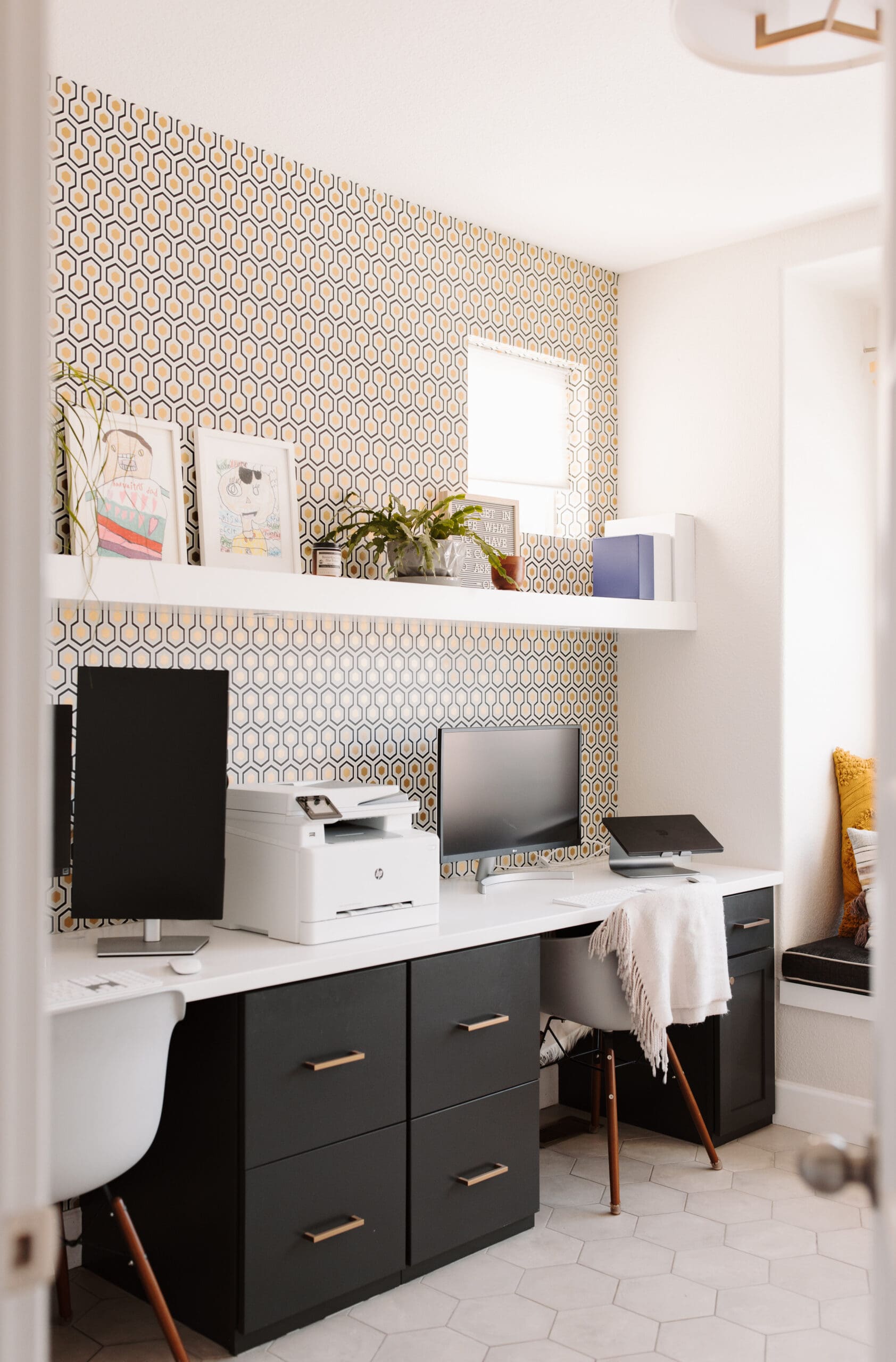 Office with natural light, geometric metallic wallpaper, charcoal cabinetry, and a white box shelf