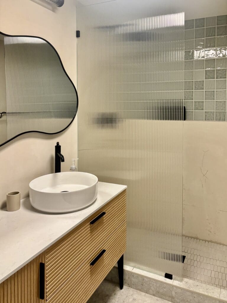 Basement bathroom with modern wood vanity, Tadelakt shower walls, and green accent tile