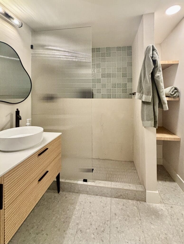 Basement bathroom with modern wood vanity, Tadelakt shower walls, and green accent tile